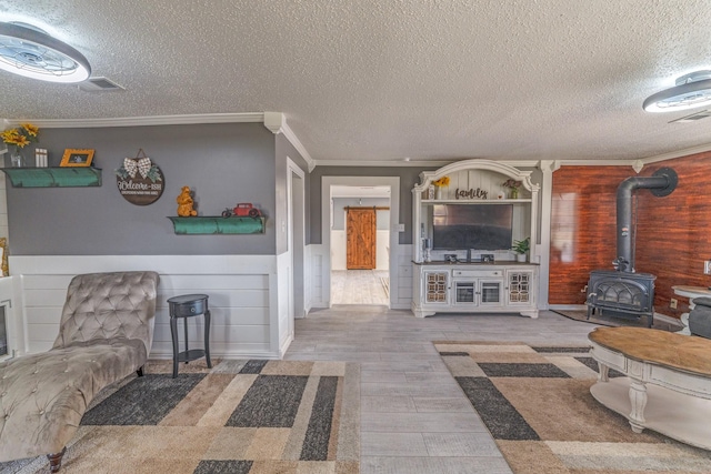 living area with visible vents, wainscoting, wood finished floors, a wood stove, and crown molding