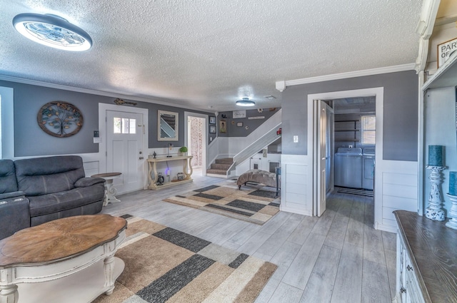 living room with crown molding, washer and clothes dryer, stairway, wainscoting, and wood finished floors