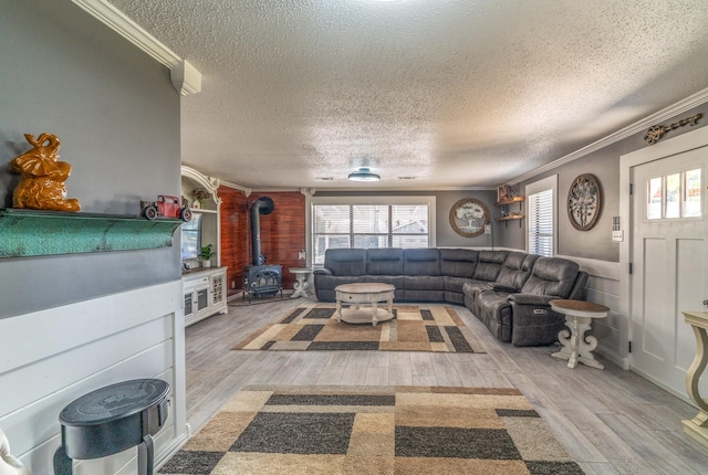 living room with light wood-style floors, a wood stove, ornamental molding, and a textured ceiling