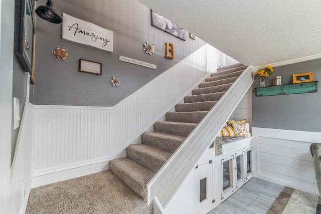 stairs with a wainscoted wall and a textured ceiling