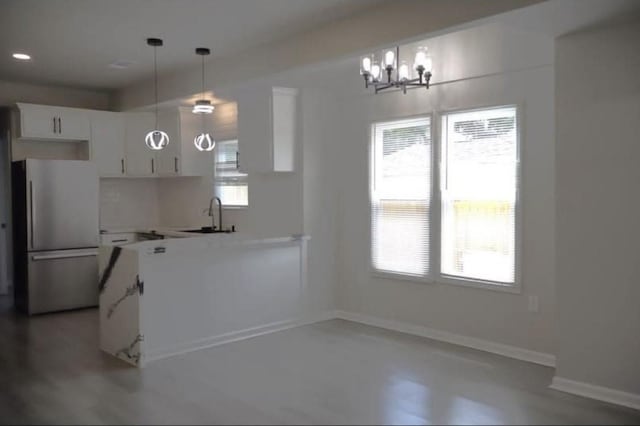 kitchen with sink, a notable chandelier, stainless steel fridge, pendant lighting, and white cabinets