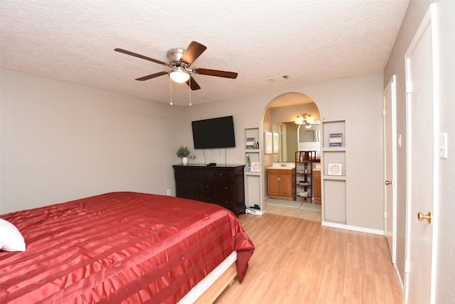 bedroom featuring ensuite bath, ceiling fan, a textured ceiling, and light wood-type flooring