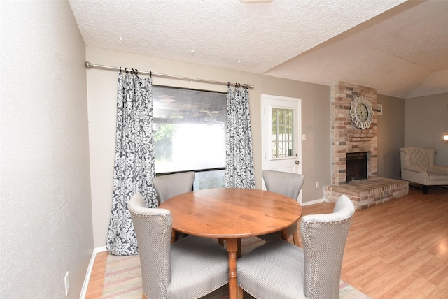 dining room with a fireplace, light hardwood / wood-style flooring, and a textured ceiling