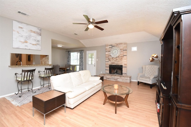 living room with ceiling fan, light hardwood / wood-style flooring, a textured ceiling, and a brick fireplace