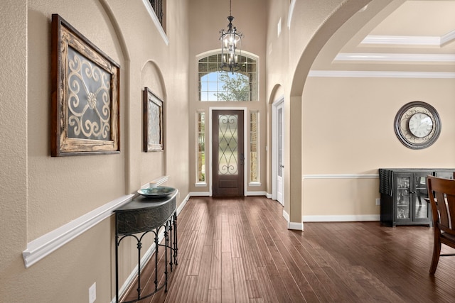 foyer entrance featuring dark wood-type flooring, ornamental molding, a towering ceiling, a tray ceiling, and a notable chandelier