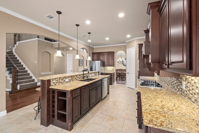 kitchen featuring a large island with sink, sink, hanging light fixtures, dark brown cabinets, and a kitchen bar