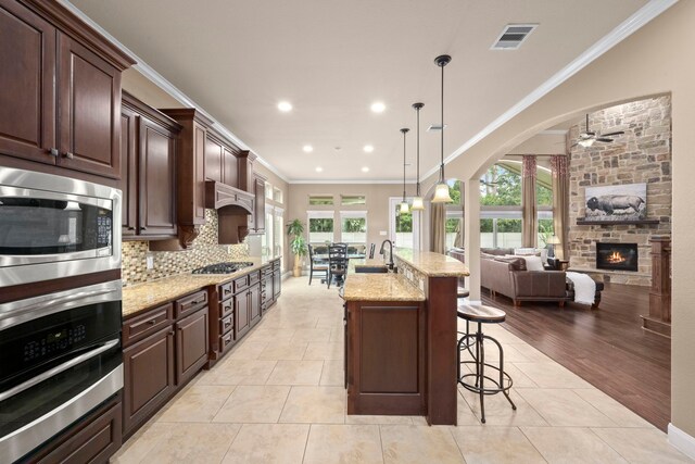 kitchen with appliances with stainless steel finishes, light wood-type flooring, crown molding, a center island with sink, and hanging light fixtures