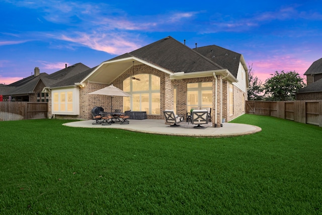 back house at dusk with ceiling fan, a patio area, and a lawn