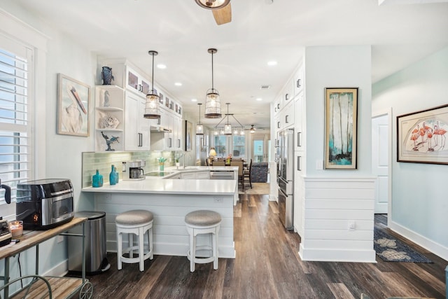 kitchen with kitchen peninsula, a kitchen bar, tasteful backsplash, dark wood-type flooring, and white cabinetry