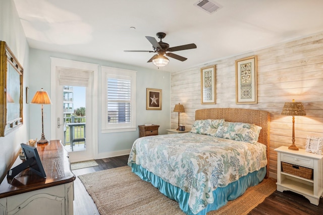 bedroom with access to exterior, dark hardwood / wood-style floors, ceiling fan, and wood walls