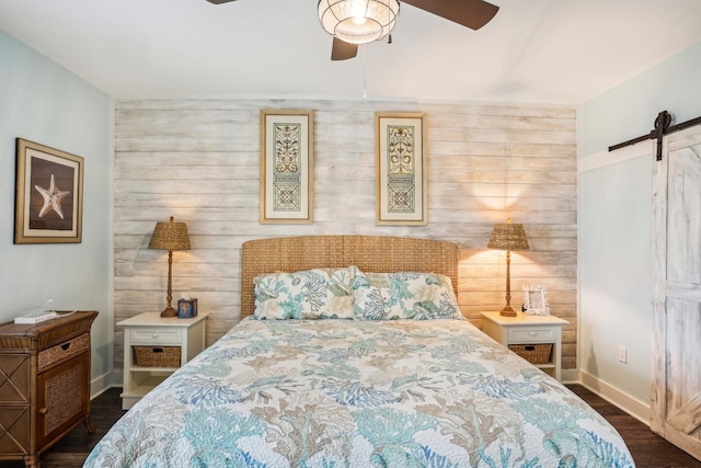 bedroom featuring a barn door, ceiling fan, dark wood-type flooring, and wood walls