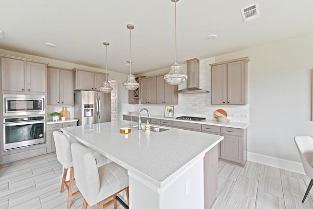 kitchen with stainless steel appliances, sink, wall chimney range hood, pendant lighting, and a center island with sink