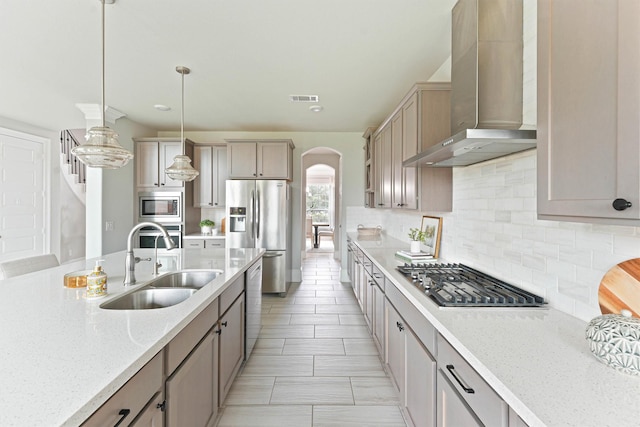 kitchen featuring light stone counters, wall chimney exhaust hood, stainless steel appliances, sink, and pendant lighting