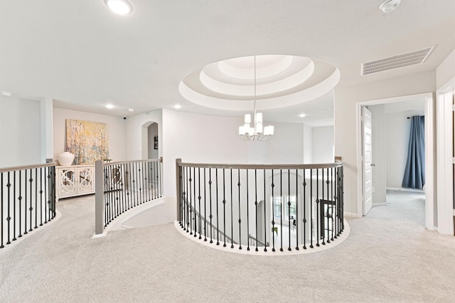 hall featuring a raised ceiling, light carpet, and a chandelier