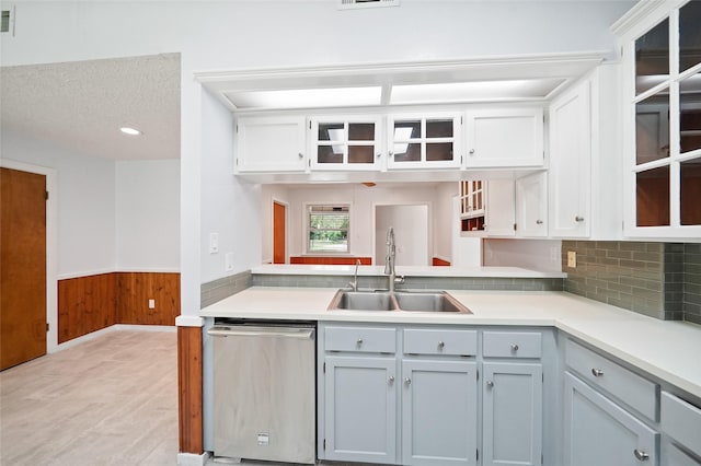 kitchen featuring backsplash, stainless steel dishwasher, a textured ceiling, wooden walls, and sink