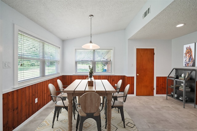 dining room with wood walls, a textured ceiling, and vaulted ceiling