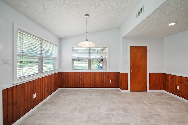 unfurnished room featuring a textured ceiling, wooden walls, and vaulted ceiling