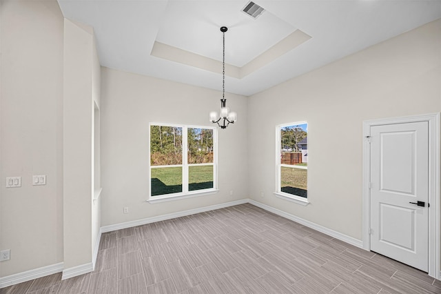 empty room featuring a raised ceiling, light hardwood / wood-style flooring, and a notable chandelier