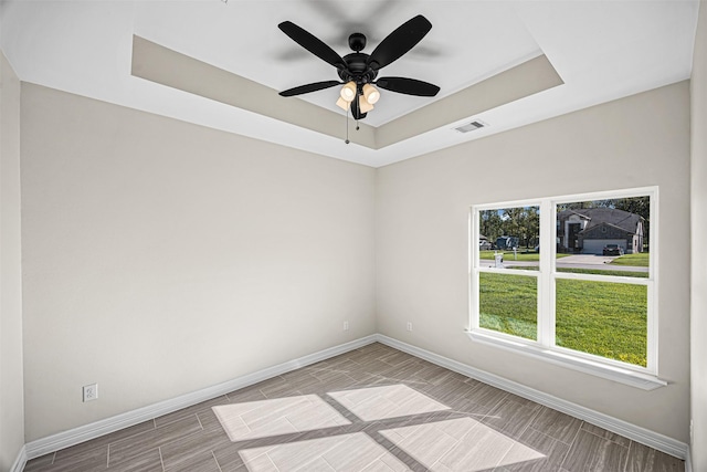 spare room with a raised ceiling, ceiling fan, and light wood-type flooring