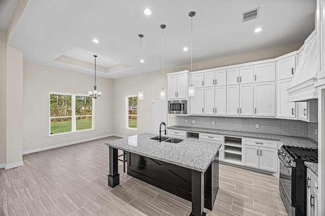 kitchen with stainless steel appliances, sink, decorative light fixtures, a center island with sink, and white cabinetry