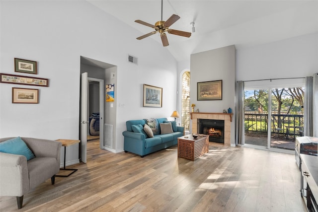 living room featuring a tile fireplace, ceiling fan, light hardwood / wood-style flooring, and high vaulted ceiling