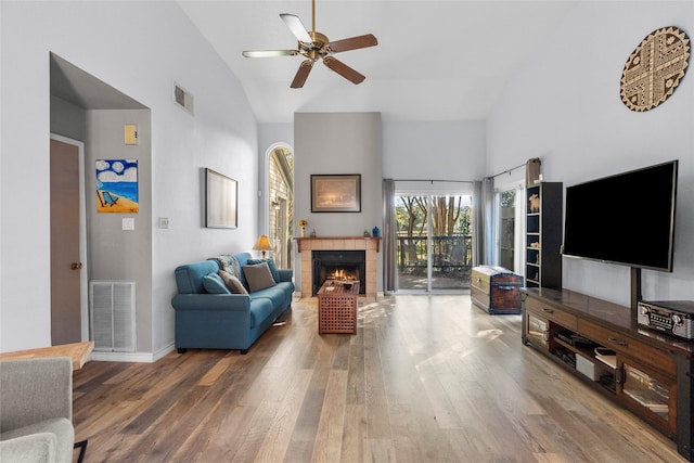 living room with hardwood / wood-style flooring, high vaulted ceiling, ceiling fan, and a tiled fireplace