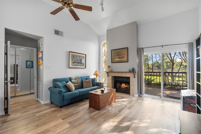 living room featuring hardwood / wood-style flooring, high vaulted ceiling, and a tiled fireplace