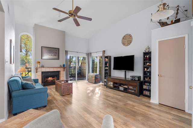 living room with a tile fireplace, ceiling fan, light hardwood / wood-style flooring, and high vaulted ceiling