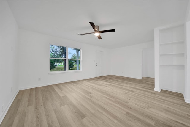 unfurnished room featuring built in shelves, light wood-type flooring, and ceiling fan