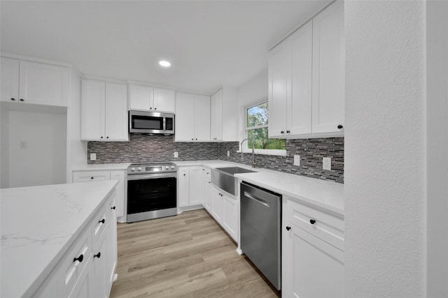 kitchen featuring sink, light stone countertops, light wood-type flooring, white cabinetry, and stainless steel appliances