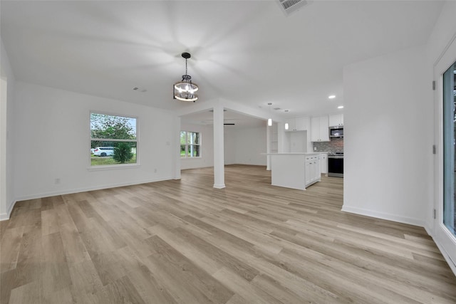 unfurnished living room featuring light wood-type flooring and an inviting chandelier