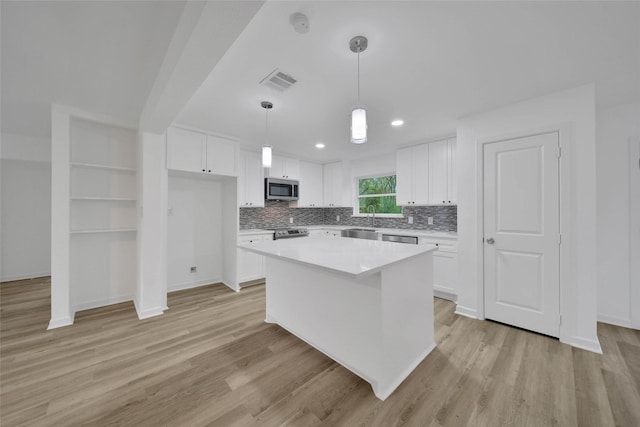 kitchen with a center island, white cabinetry, hanging light fixtures, and appliances with stainless steel finishes