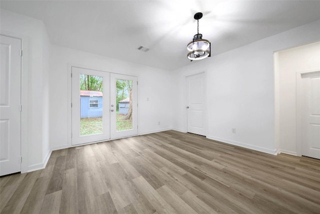 unfurnished room with a chandelier, light hardwood / wood-style floors, and french doors