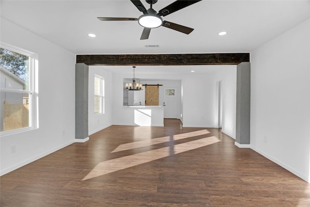 unfurnished living room with ceiling fan with notable chandelier, beam ceiling, a barn door, and dark wood-type flooring