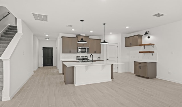 kitchen featuring a kitchen island with sink, hanging light fixtures, light hardwood / wood-style flooring, and stainless steel appliances