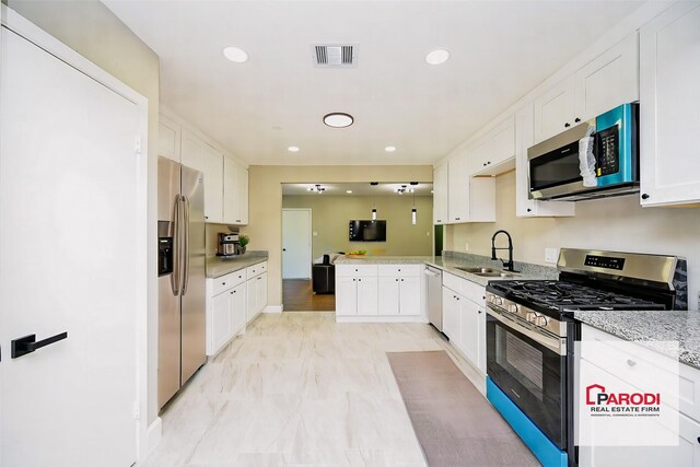 kitchen with kitchen peninsula, appliances with stainless steel finishes, light stone counters, sink, and white cabinets