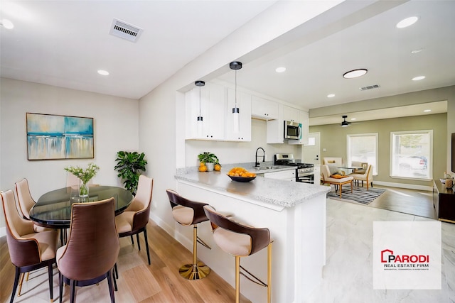 kitchen with white cabinetry, kitchen peninsula, decorative light fixtures, appliances with stainless steel finishes, and light wood-type flooring