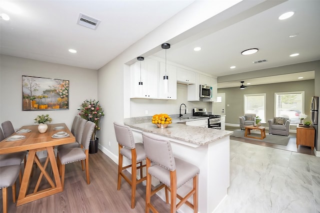 kitchen with pendant lighting, appliances with stainless steel finishes, a kitchen breakfast bar, light stone countertops, and white cabinets