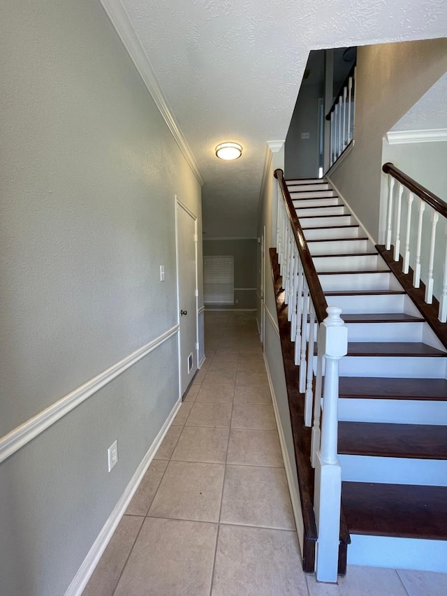 stairway with tile patterned floors, crown molding, and a textured ceiling