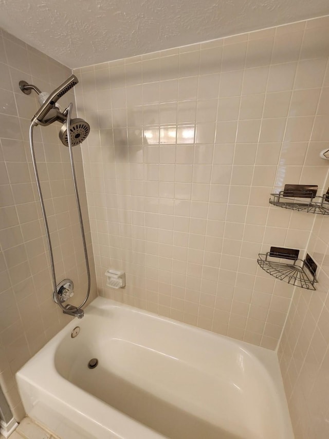 bathroom with a textured ceiling and tiled shower / bath