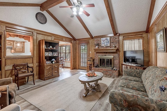 living room featuring a textured ceiling, wooden walls, beam ceiling, light hardwood / wood-style flooring, and a fireplace