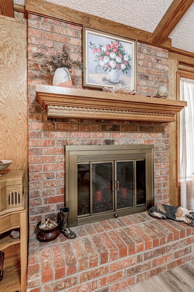 interior details featuring a fireplace, beamed ceiling, wood-type flooring, and a textured ceiling