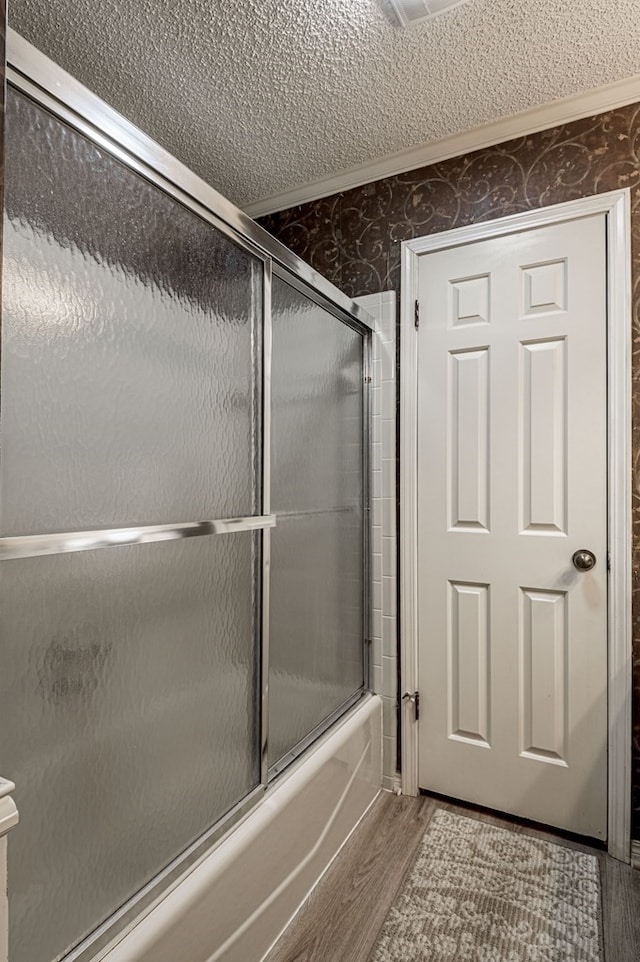 bathroom with hardwood / wood-style floors, a textured ceiling, and enclosed tub / shower combo