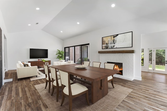 dining space with a fireplace, high vaulted ceiling, and hardwood / wood-style flooring