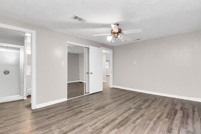 unfurnished bedroom featuring a closet, ensuite bath, ceiling fan, and dark wood-type flooring