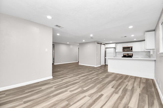 unfurnished living room with a textured ceiling, a barn door, light hardwood / wood-style flooring, and sink