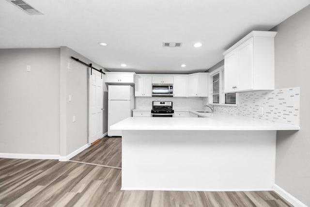 kitchen with a barn door, white cabinetry, kitchen peninsula, and stainless steel appliances