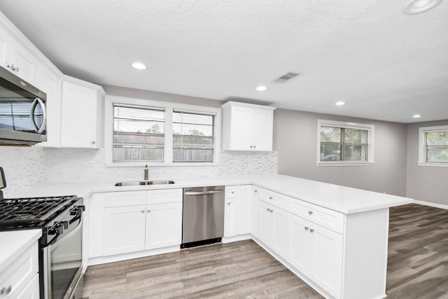 kitchen featuring sink, light hardwood / wood-style flooring, kitchen peninsula, white cabinets, and appliances with stainless steel finishes