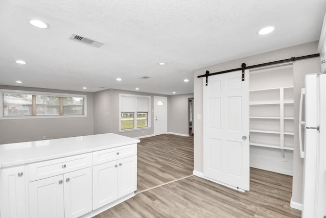 kitchen featuring white cabinets, a barn door, light wood-type flooring, a textured ceiling, and white fridge