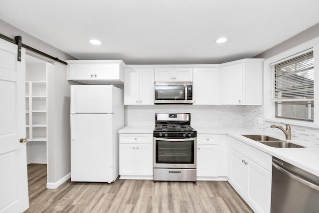 kitchen with appliances with stainless steel finishes, backsplash, sink, a barn door, and light hardwood / wood-style flooring